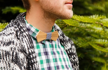 Young fashion styled man in wooden bowtie and plaid shirt in front of nature backgroundの写真素材