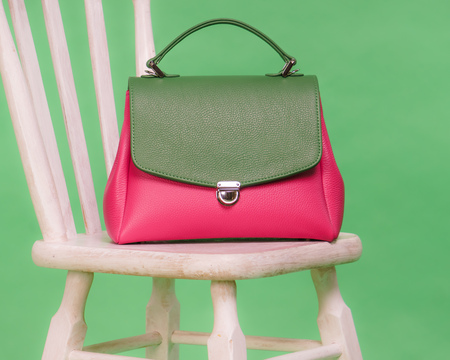 Fashion styled womans handbag in pink and green colors standing on a wooden chair on green backgroundの写真素材