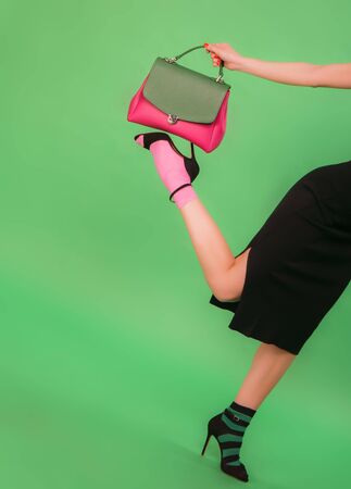 Fashion styled woman holding womans handbag on a foot on green backgroundの写真素材