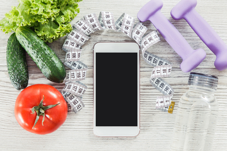 Mobile phone with vegetables, measure tape, water and dubmb-bell on the wooden tableの写真素材
