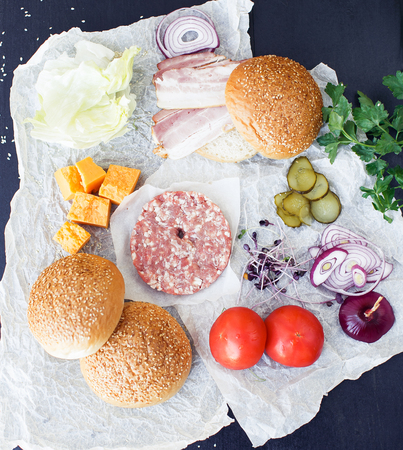 Raw ingredients for burger on butter-paper and black backgroundの写真素材
