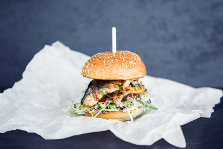 Freshmade streetfood fishburger on the butter-paper on the black backgroundの写真素材