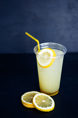 Lemon lemonade in the plastic cup on the black backgroundの写真素材