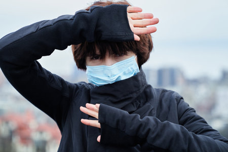 Fashion styled distressed young woman in medical mask with blurred city view backgroundの写真素材