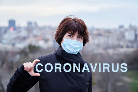 Young woman in medical mask and casual wear against corona virus with city backgroundの写真素材