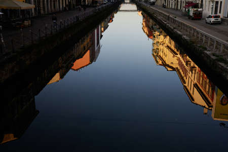 Image of the beautiful architectural yellow building with balconies as a reflection on the water in canal in Milan historical city center in early morningの写真素材