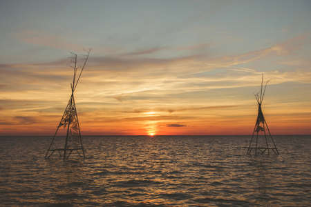 Silhouettes of tree sticks construction in the water with beautiful tranquil summer scene of orange...
