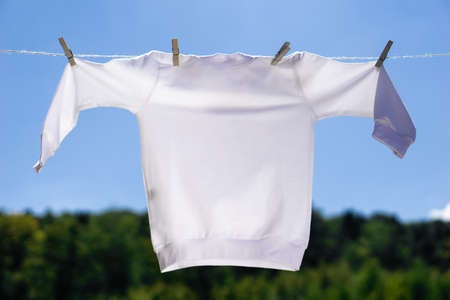 White pullover mockup hanging in front of blue sky and green trees background. Sweater is hanging on a rope with clothespins. Mock-up summer concept.の写真素材