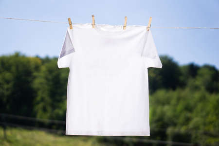 White t-shirt mock-up hanging on the rope with clothespins on summer background. Mockup ready to...