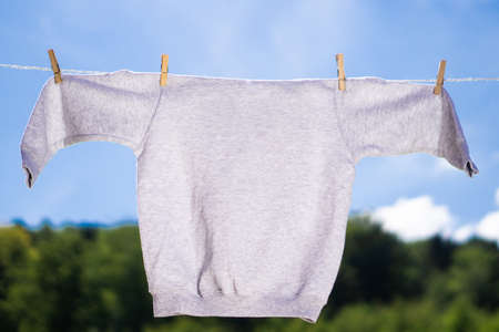 Sweater grey mock-up hanging on the rope with clothespins in front of blue sky and green trees summer background. Mockup concept.の写真素材