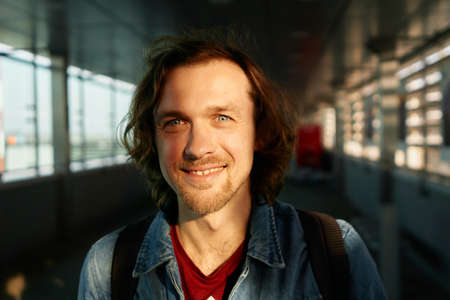 Portrait of young smiling man in casual clothes on sunset airport background looking straight in...