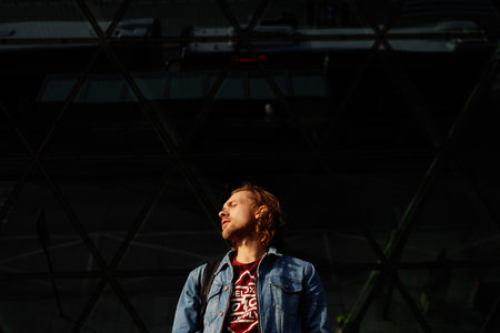 Portrait of stylish tourist man in t-shirt and jeans jacket in light sunset background looking back...