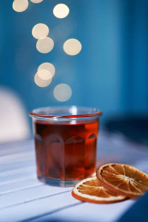 Tea in glass with orange slices on the table and blue background with blurred lights. Tea time or...