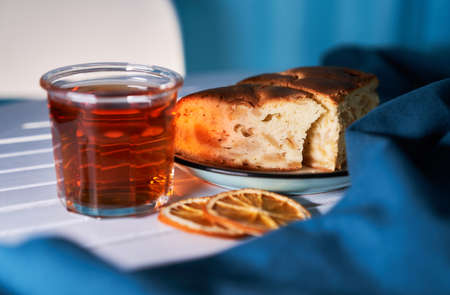Tea in the glass with apple pie and orange on the white table with blue background. Tea time concept.の写真素材