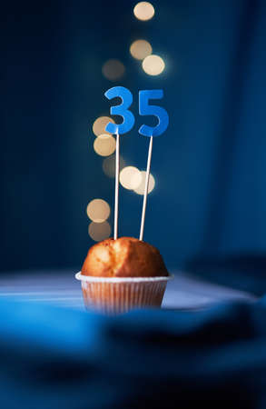 Birthday cake or muffin with thirty five (35) number and blurred lights on the blue background. Birthday or anniversary conceptの写真素材