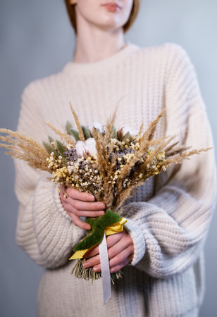 Attractive young girl holding beautiful flowers bouquet of dry hydrangea, cotton, eucalyptus in orange and brown colors on the flower shop. Boho style bouquetの写真素材