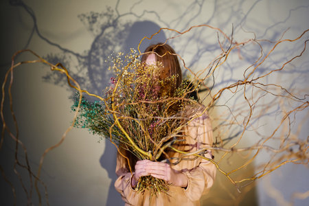 Young beautiful girl in pink blouse holding in her hands a huge flower bouquet of tree branches decorated with dried flowers. Spring time conceptの写真素材