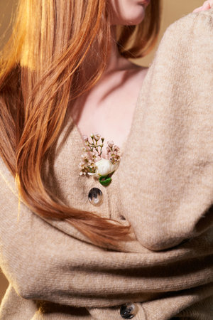 Attractive long ginger colored hair girl in sweater with a small bouquet of fresh flowers in the neckline. Tenderness, sensitive and love vibe conceptの写真素材