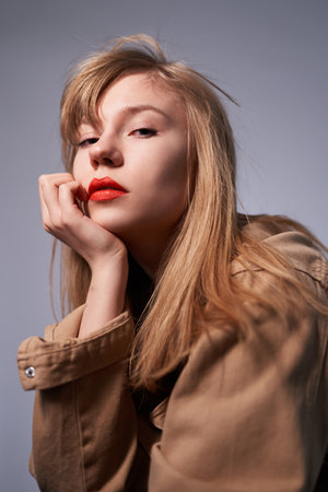 Fashion portrait of elegant blonde woman with bright makeup looking straight in camera. Beautiful blonde with red lipstick on her lips. Pretty girl with long blonde hair dressed in a beige jacketの写真素材