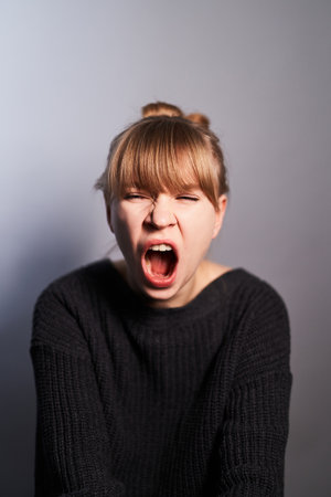 Portrait of young yawning woman wearing black sweater isolated on gray background. Expressions conceptの写真素材