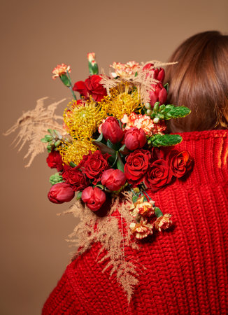 Attractive girl in red sweater holding colored bouquet of beautiful roses, tulips, carnation flowers behind her back. St. Valentine's Day, International Women's Day or Mother's Day conceptの写真素材
