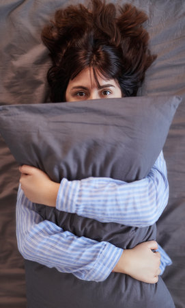 Closeup portrait of brunette woman with gray pillow in arms on gray background. Relax in the bedroom in the morning or evening. Concept of lazy sunday in a bedの写真素材