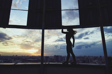 High level concept. Silhouette of standing alpinist woman standing on the top of the building with sunset sky with clouds backgroundの写真素材