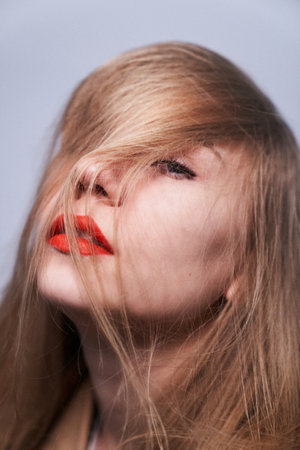 Studio beauty portrait of a blonde girl with fashion make-up, long hair and red lipstick isolated on gray backgroundの写真素材