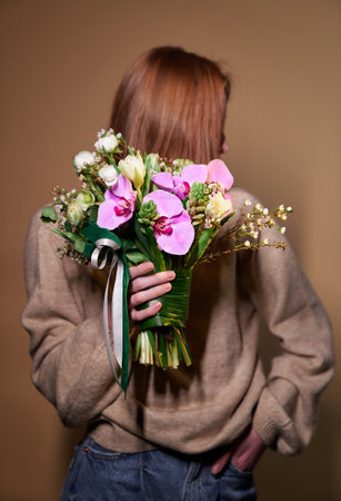 Stylish beautiful girl in beige sweater and jeans with a flowers, covered her face with a bouquet, spring theme. Mother's Day, St. Valentine's day or International Woman's Day conceptの写真素材