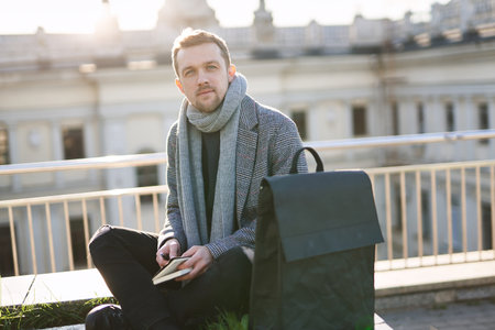 Young attractive man in scarf and coat looking at the camera, sitting with the note. Working or...