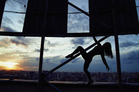 Silhouette of alpinist female climbing high risk building against a blue cloudy sky for the concept of urban playground and city viewの写真素材