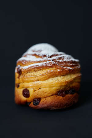 Cute cruffin with raisins and white sugar powder on it on black background. Fresh Easter pie or bakery concept. High quality photoの写真素材
