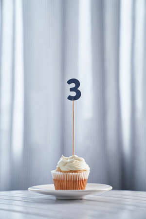Anniversary or birthday minimalistic greeting card concept. Tasty vanilla cupcake or muffin with...