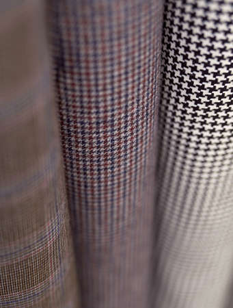 Closeup stack of warm wooled tweed textile rolls with different patterns. Sale or tailoring objects...