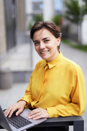 Closeup portrait of happy skilled successful young 30s business lady staying at the street with laptop, looking at camera. Female entrepreneur working outside office building. High quality imageの写真素材