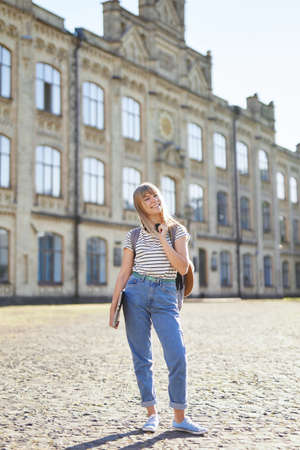 Attractive happy young blonde high school girl or college student with backpack and laptop wearing...