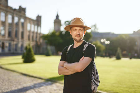 Cheerful man traveler in hat and backpack with European city center background. Travel and old city...