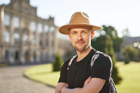 Travel and old city explore concept. Cheerful man traveler in hat and backpack in European city...