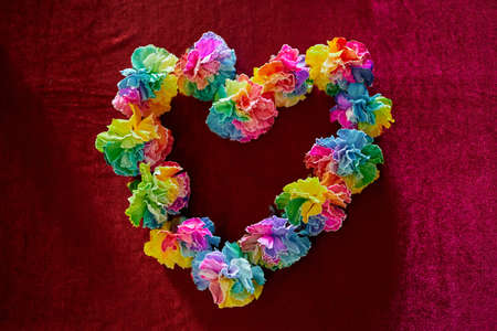 Beautiful heart made of colorful carnation flowers on red background. Can be used as symbol of LGBTQ or Mothers Day holiday. Rainbow color flowers in heart shape. High quality photoの写真素材