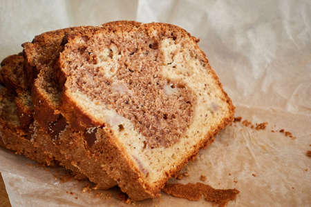 Tasty homemade food concept. Freshly baked sweet pastry bread loaf on gray baking paper cutted into...