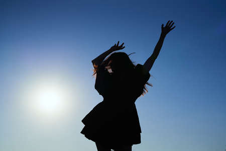 Attractive caucasian elegant girl in dress dancing during sunset or woman performing modern dance outdoor in sunny day against blue sky. Silhouette dance. High quality imageの写真素材
