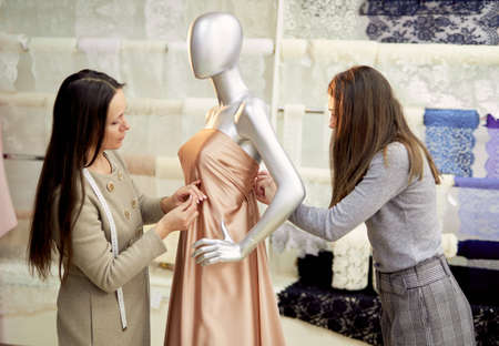Professional brunette team of tailors, dressmakers or designers working with new model applying linen fabrics cloth on mannequin or dummy in atelier. Fashion and tailoring concept. High quality imageの写真素材