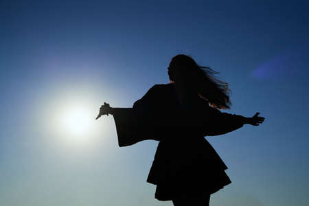 Attractive caucasian elegant girl in dress dancing during sunset or woman performing modern dance outdoor in sunny day against blue sky. Silhouette dance. High quality imageの写真素材