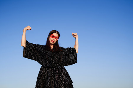 Female power, women rights, feminism activist concept. Portrait of strong woman in black dress and red face mask making fist pump, protesting for freedom and equality outdoor. High quality photoの写真素材