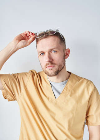 Close up portrait of a male doctor or nurse with his arms raising up eyeglasses. Professional caucasian doctor at hospital. Medical healthcare business and doctor service concept. High quality photoの写真素材