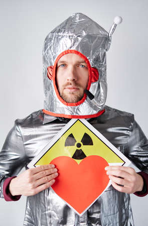 Portrait of young bearded astronaut man standing by the white wall holding red heart shape and...