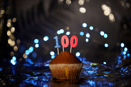Tasty homemade vanilla anniversary cupcake with number 100 one hundred on aluminium foil and blurred bright background in minimalistic style. Digital gift card birthday concept. High quality imageの写真素材