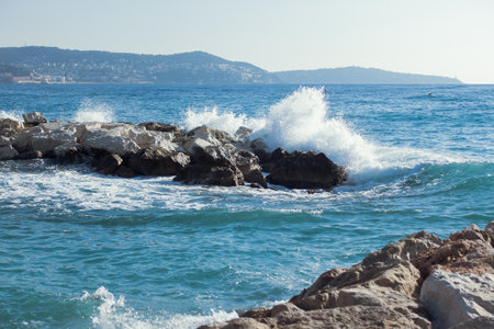 Water splashing while powerful waves crushing into the rocks in the Mediterranean sea coast with mountains on background. Nature, vacation or summer concept. High quality photoの写真素材