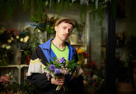 Congratulating with flowers: portrait of man in peaked cap and tracksuit holding spring flower...