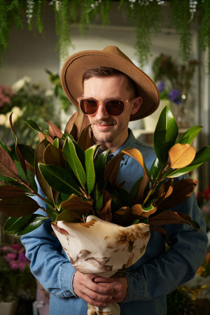 Cute caucasian hipster person in sunglasses and hat holding big fresh spring flower bouquet in flower shop. Mothers Day, Valentines Day or International Womens Day concept. High quality imageの写真素材